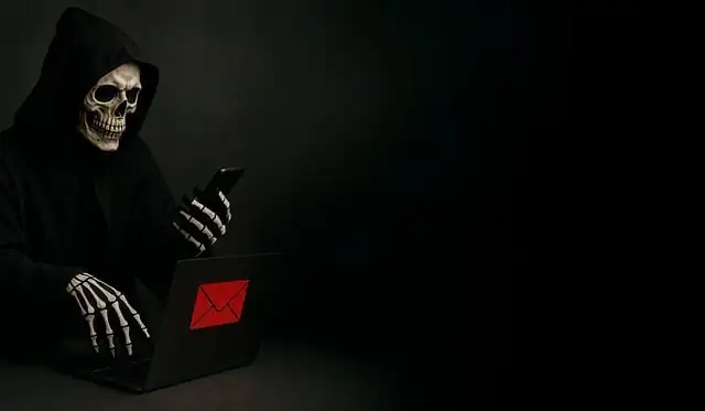 Person in skeleton costume in front of a laptop and holding a mobile phone.