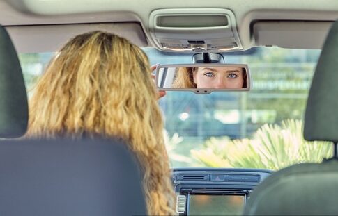 Blonde woman with blue eyes looking in a car's rearview mirror