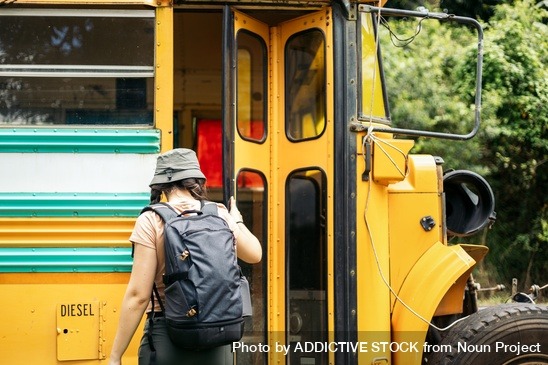 Girl wearing a hat and backpack about to board a bus.