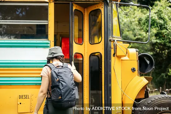 Girl wearing a hat and backpack about to board a bus.